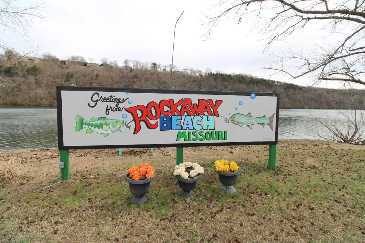 A friendly lakeside entrance scene with a welcoming sign, flower pots, and a clear view of the lake beyond. The setting feels inviting and hints at the experiences awaiting guests, like fishing, nature walks, and memorable outdoor moments.