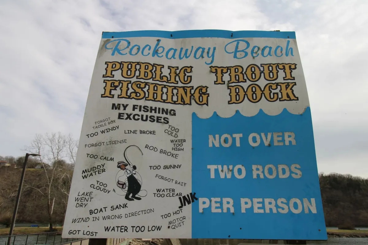 The hero image shows a playful fishing dock sign adorned with colorful graphics and a list of humorous fishing excuses, set against the backdrop of a sunny lakeside scene. The atmosphere is lively and welcoming, inviting guests to enjoy fishing, outdoor meals, and socializing by the water.