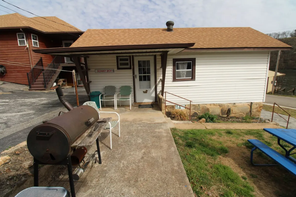 The entrance to the cabin, highlighted by an outdoor seating area and a grill. The scene suggests a transition from the comfort of the cabin to the outdoor environment, ideal for both relaxation and preparation before hitting the water.