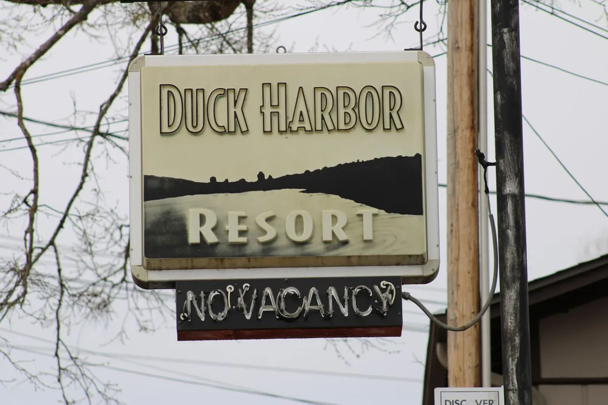This image shows the welcoming neon signage of Duck Harbor Resort set against a natural landscape, likely at sunset. The glow creates a cozy, inviting atmosphere and hints at the resort’s proximity to the water and nature.