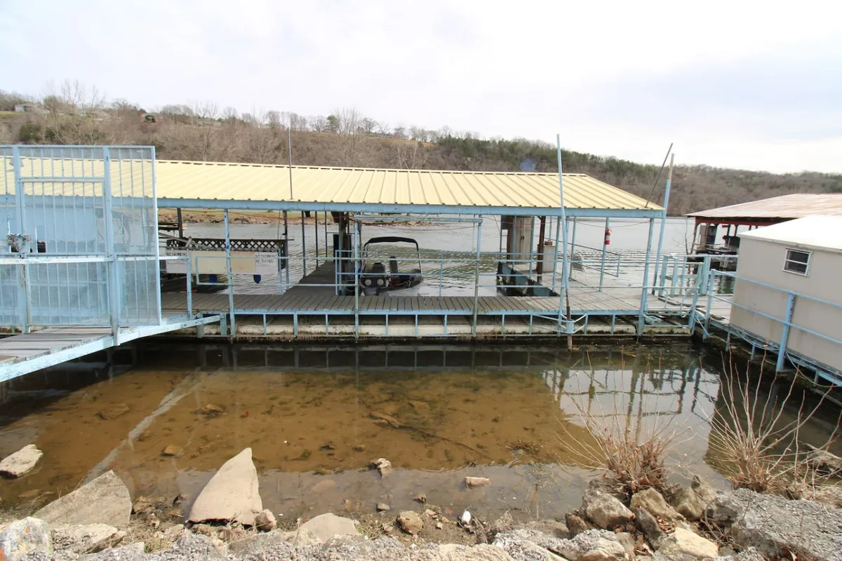 A peaceful dock stretches out over Lake Taneycomo, surrounded by serene water and natural landscape. The dock appears ready for boating or fishing activities, with the tranquil lake surface inviting an early start to the day.